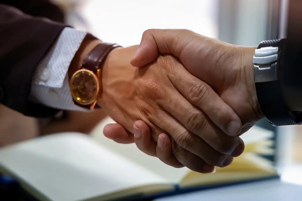 Two business partners shaking hands over a table, symbolizing agreement and collaboration.